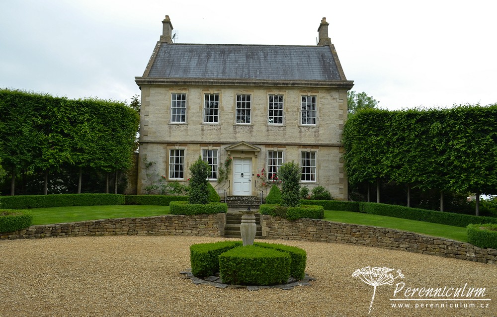 Příběh zahrady v Doyntonu 5 Reprezentativní prostor před domem tvoří kruhová příjezdová cesta s výrazným schodištěm ke vstupním dveřím, které rámuje sytě červená pnoucí růže.